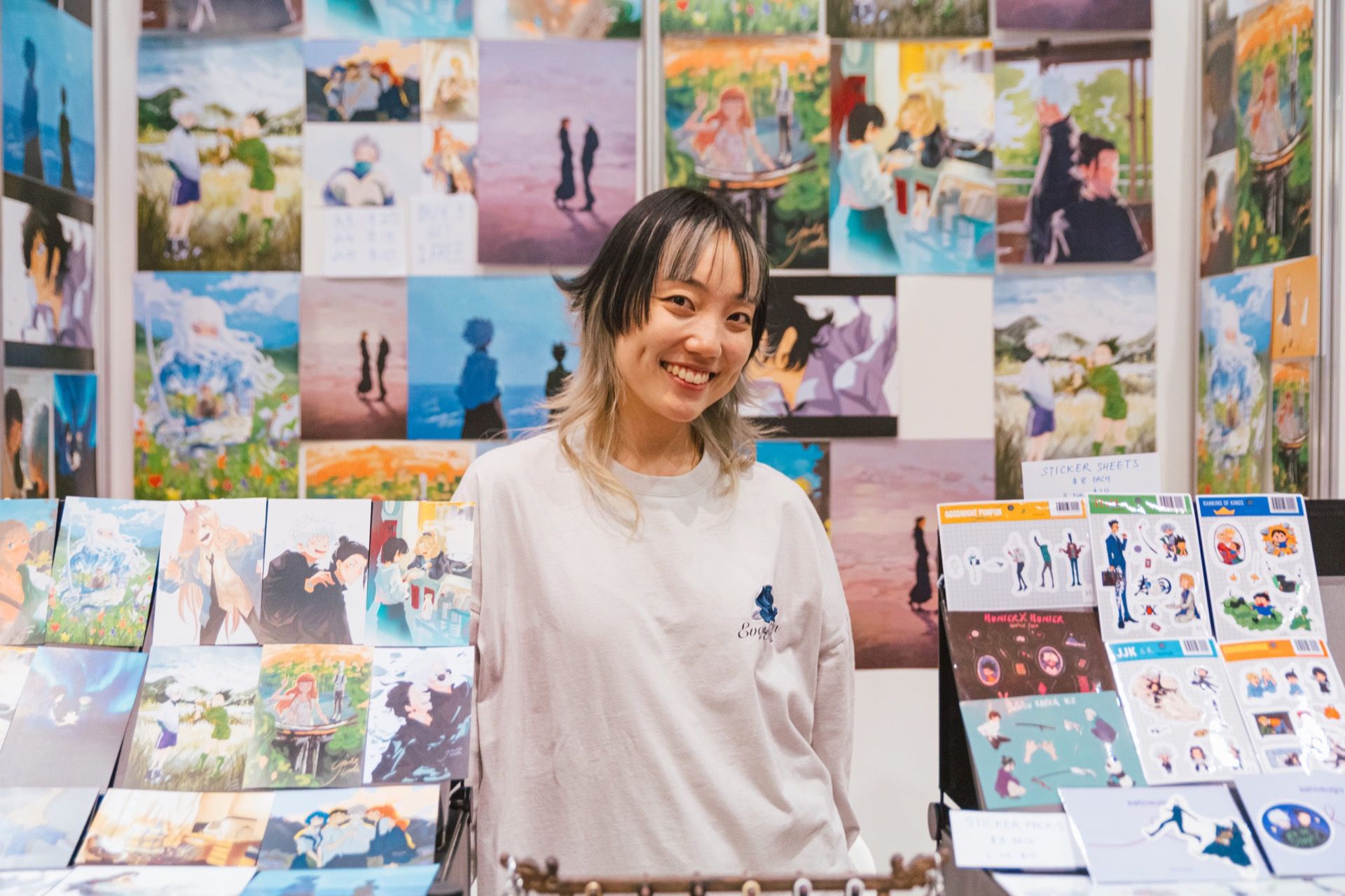 An artist smiling behind her table in the Artist Alley